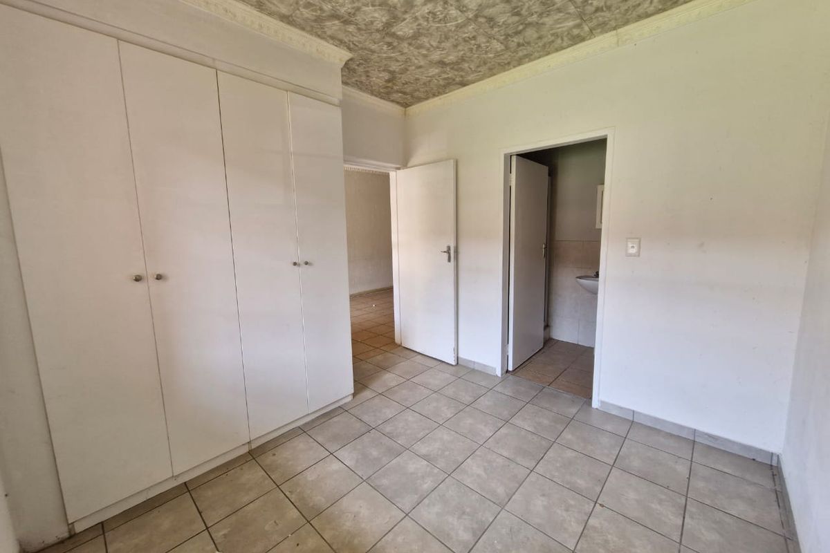 An empty bedroom featuring built-in cupboards, tiled flooring, and a textured ceiling, with an adjacent en-suite bathroom area.