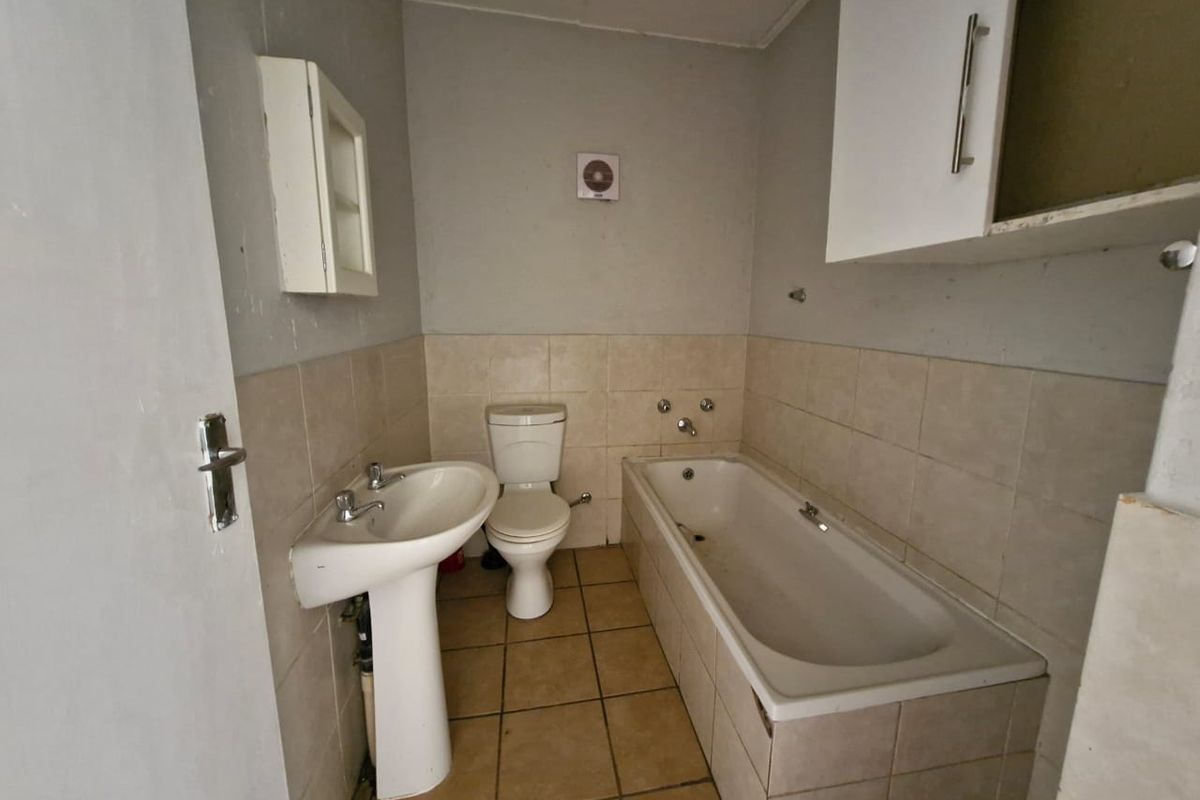 A functional bathroom featuring a pedestal basin, toilet, and bathtub with tiled finishes, requiring cosmetic updates to improve its overall condition.