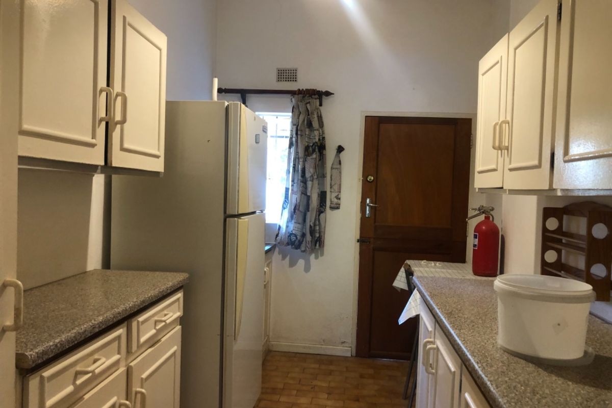 A compact kitchen featuring dated cabinetry, laminate countertops, and tiled flooring, providing a functional layout with direct access to an exterior door.