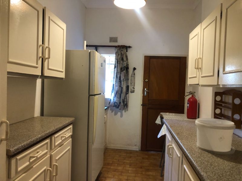 A compact kitchen featuring dated cabinetry, laminate countertops, and tiled flooring, providing a functional layout with direct access to an exterior door.