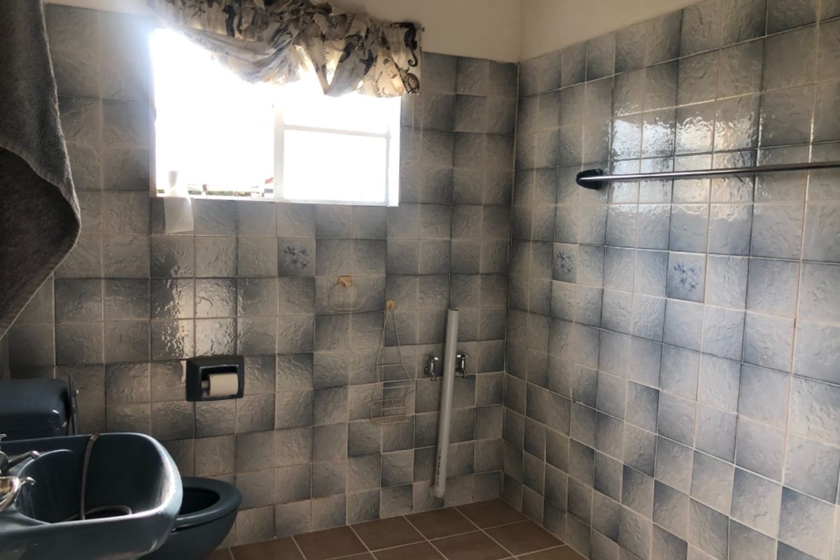 A dated bathroom featuring blue wall tiles, a tiled floor, and a basin. The space requires modernization of fixtures and finishes.