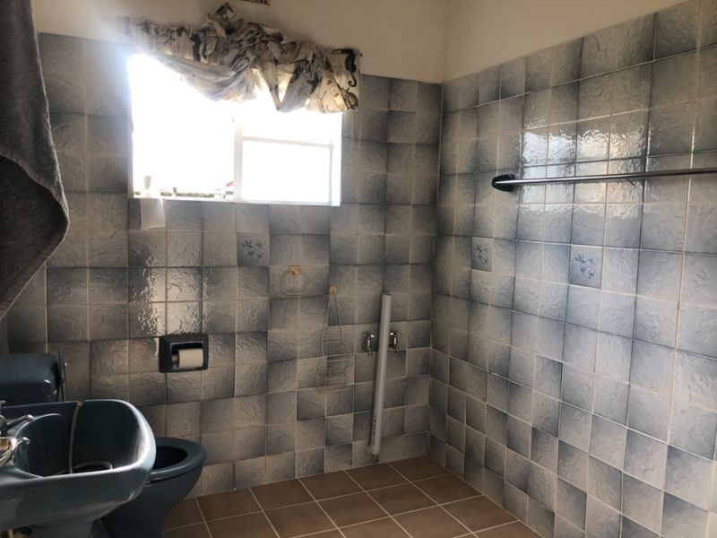 A dated bathroom featuring blue wall tiles, a tiled floor, and a basin. The space requires modernization of fixtures and finishes.