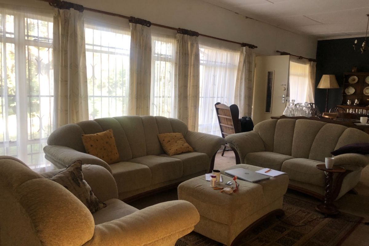 Spacious living room featuring large windows with security bars and natural light, offering a comfortable area for relaxation.