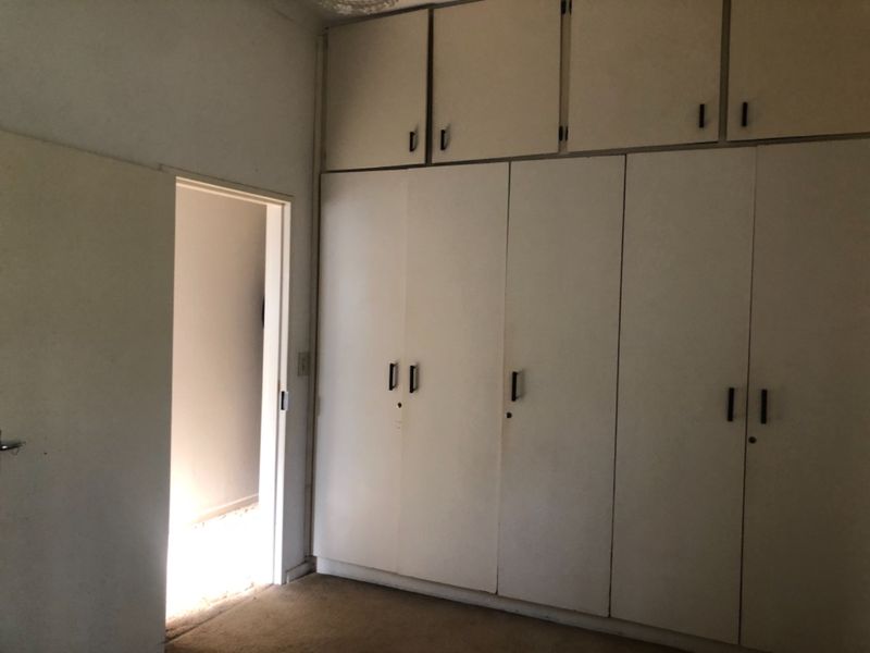 A bedroom featuring extensive floor-to-ceiling built-in cupboards and overhead storage, providing ample storage space. The room is currently vacant and ready for updates.