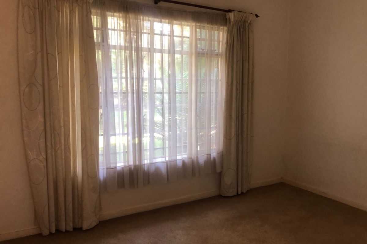 An empty bedroom featuring carpeted flooring, a large window with security bars, and neutral wall finishes, ready for a fresh update.