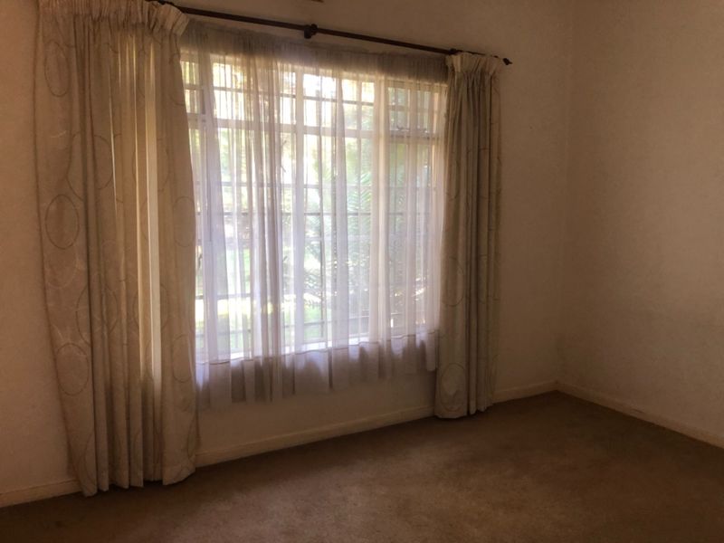 An empty bedroom featuring carpeted flooring, a large window with security bars, and neutral wall finishes, ready for a fresh update.