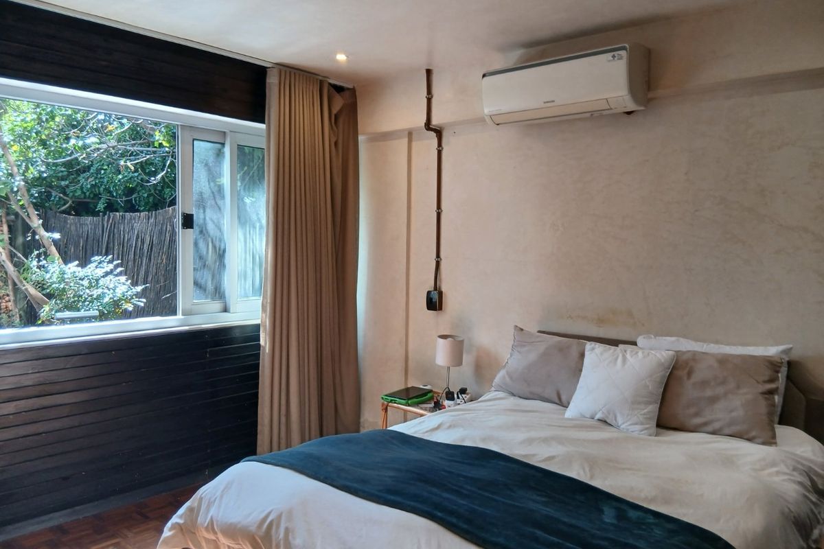 A bedroom featuring parquet flooring, recessed lighting, and a wall-mounted air conditioning unit with an exterior garden view.