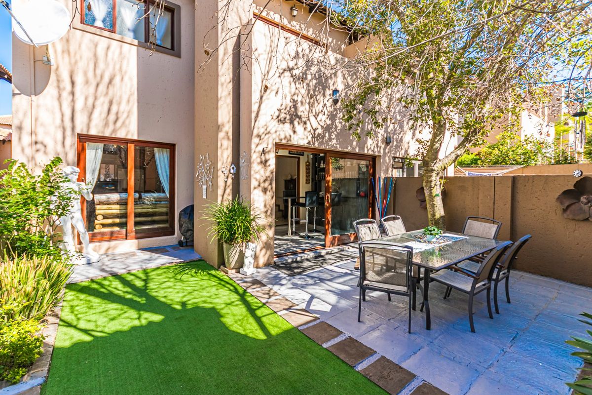 Rear exterior view of the townhouse featuring a paved patio area, artificial lawn, and sliding glass doors providing access to the interior living space.