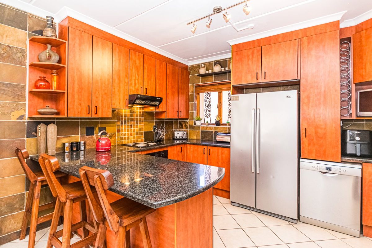 A functional kitchen featuring warm-toned wooden cabinetry, granite countertops, a breakfast bar, and tiled splashbacks, offering ample storage and workspace.