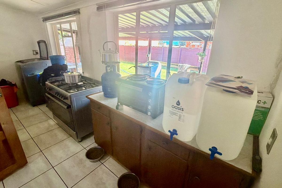 A functional kitchen area featuring wooden cabinetry, tiled flooring, and a freestanding gas stove, with direct access to the rear outdoor space.