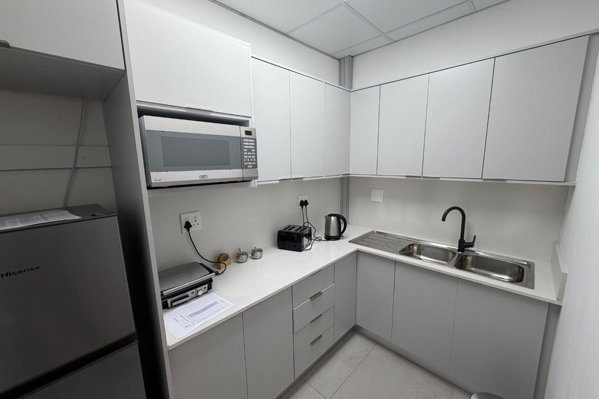 A modern, compact commercial kitchenette featuring sleek grey cabinetry, stone countertops, a double sink with a matte black tap, and a built-in microwave.