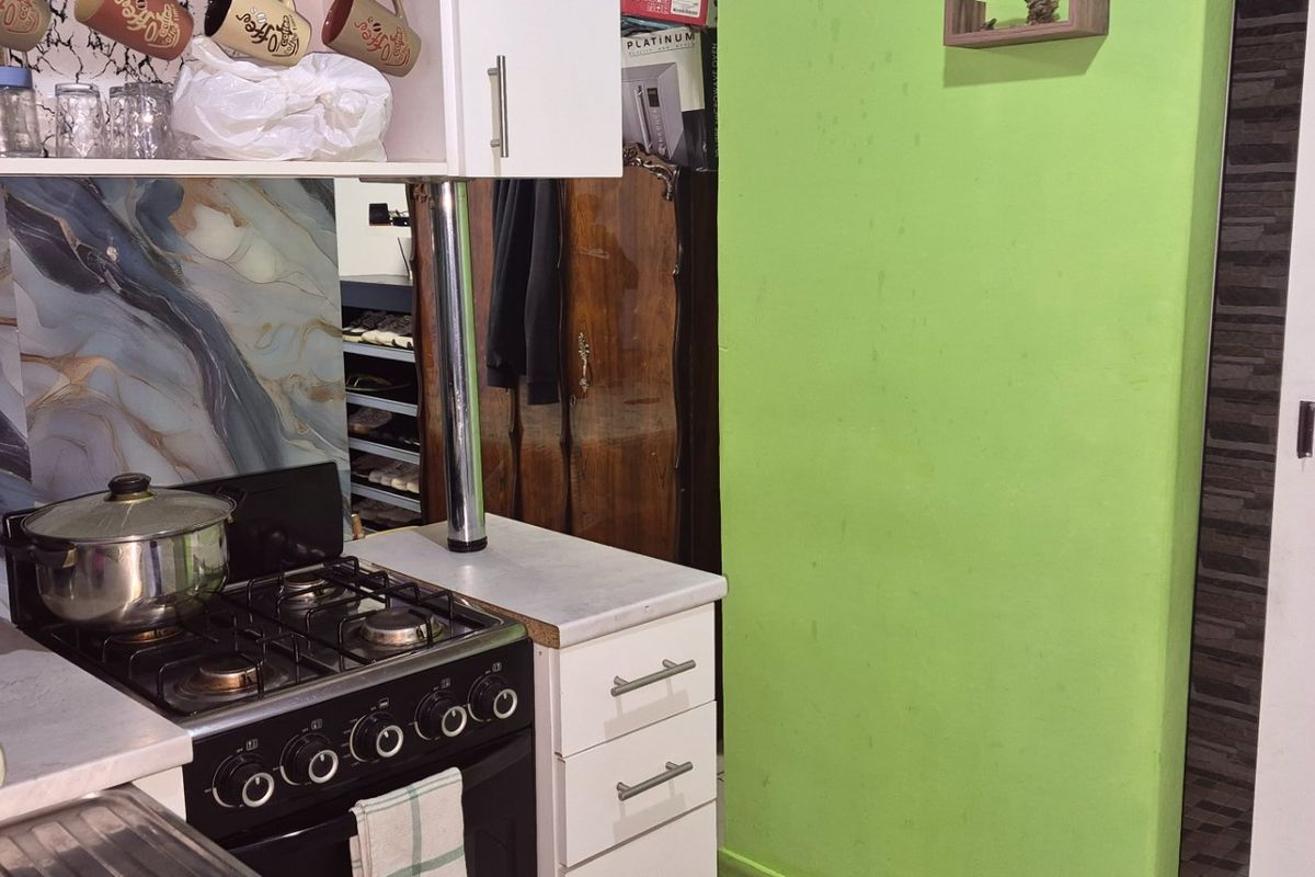 A compact kitchen area featuring built-in cabinetry, a gas stove, and a decorative marble-effect splashback, requiring cosmetic updates to improve the overall aesthetic.