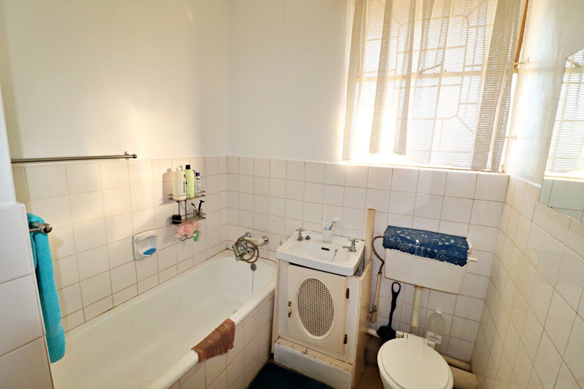 A compact bathroom featuring a bathtub, pedestal sink, and toilet with dated finishes and ceramic wall tiling.