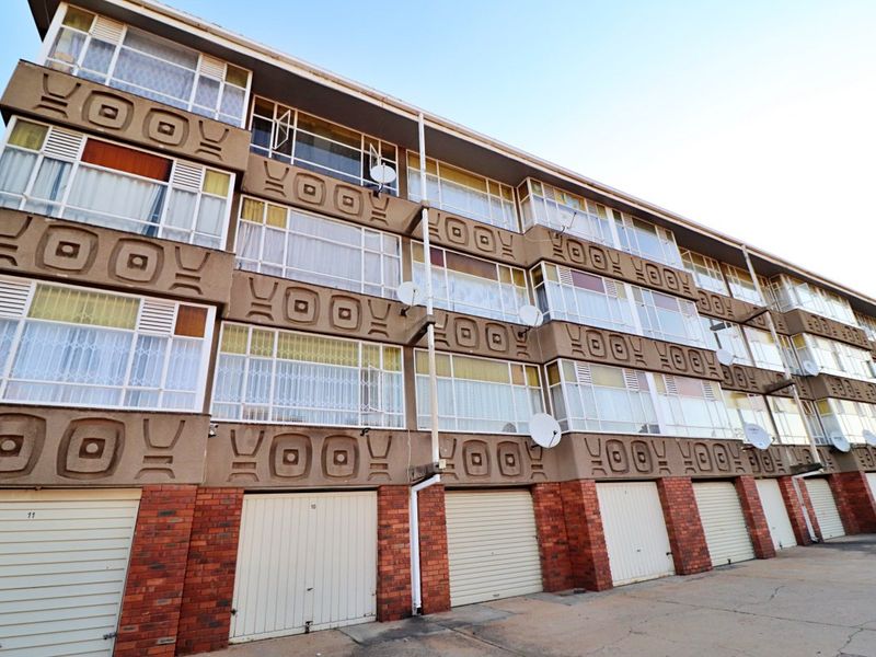 Exterior view of a multi-story apartment complex featuring brick base, decorative concrete facade panels, and ground-level roller garage doors.