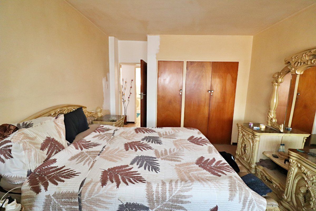 Bedroom featuring built-in wooden cupboards and access to an adjoining room, currently requiring cosmetic updates to wall finishes.