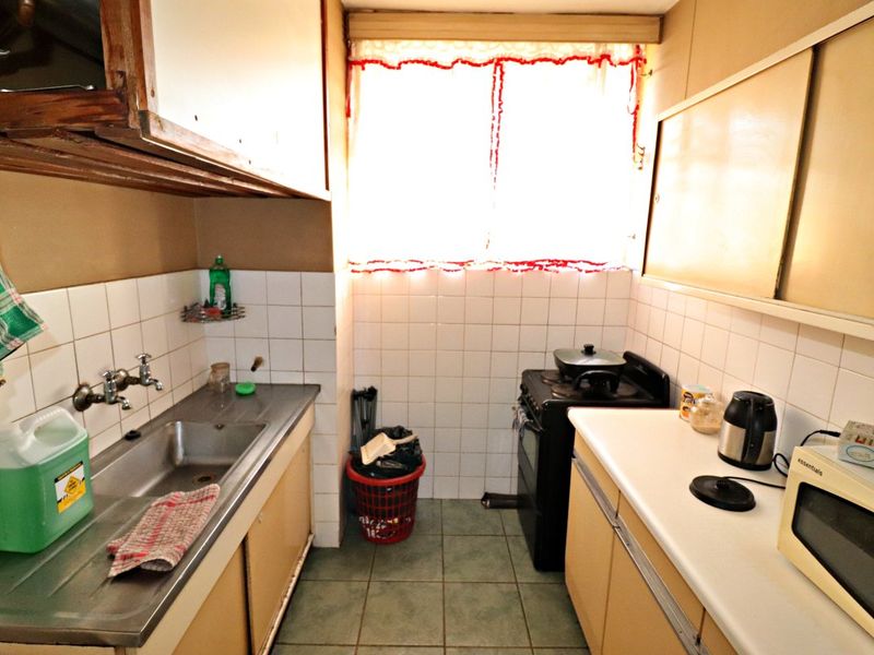 A compact, dated kitchen featuring a stainless steel sink, tiled splashbacks, and original cabinetry, offering significant potential for a modern renovation.