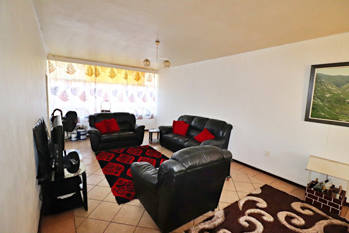 A spacious living room featuring tiled flooring, a large window allowing natural light, and a neutral wall finish.