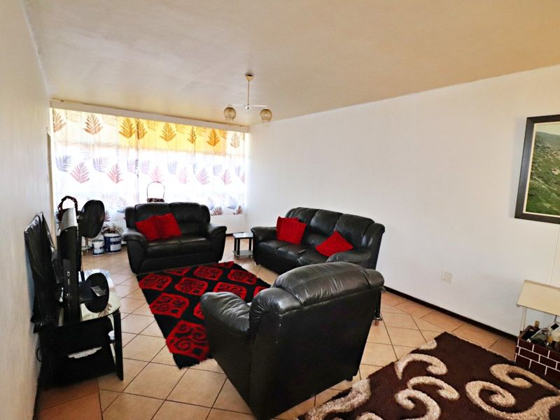 A spacious living room featuring tiled flooring, a large window allowing natural light, and a neutral wall finish.