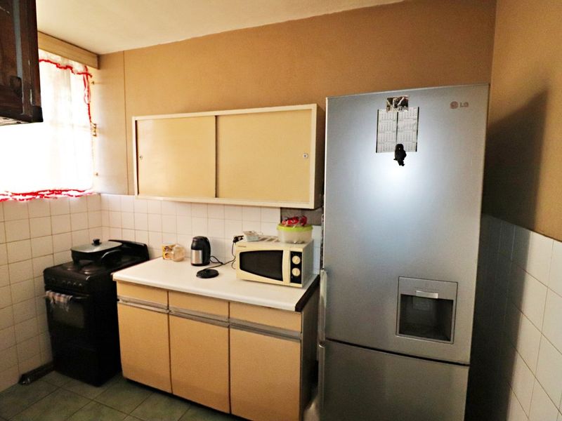 A functional kitchen featuring dated cabinetry, tiled splashbacks, and tiled flooring, offering potential for modernization and aesthetic improvement.