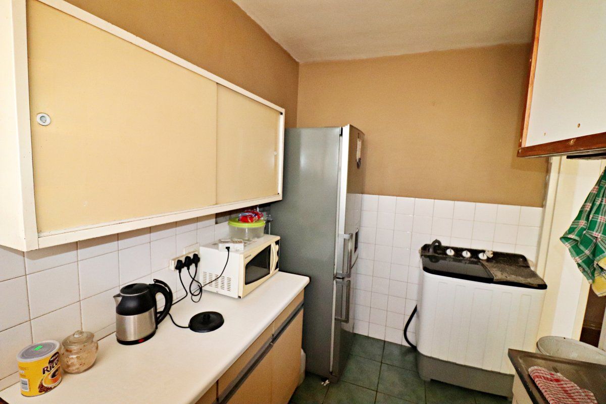 A compact kitchen featuring laminate countertops, tiled backsplash, and tiled flooring, offering a functional layout with existing cabinetry and utility space.