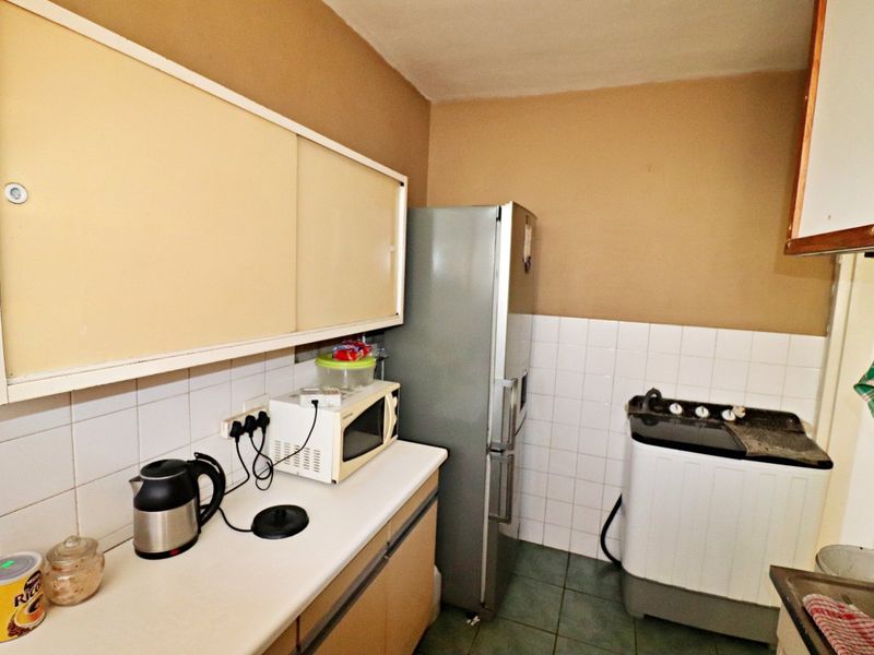A compact kitchen featuring laminate countertops, tiled backsplash, and tiled flooring, offering a functional layout with existing cabinetry and utility space.