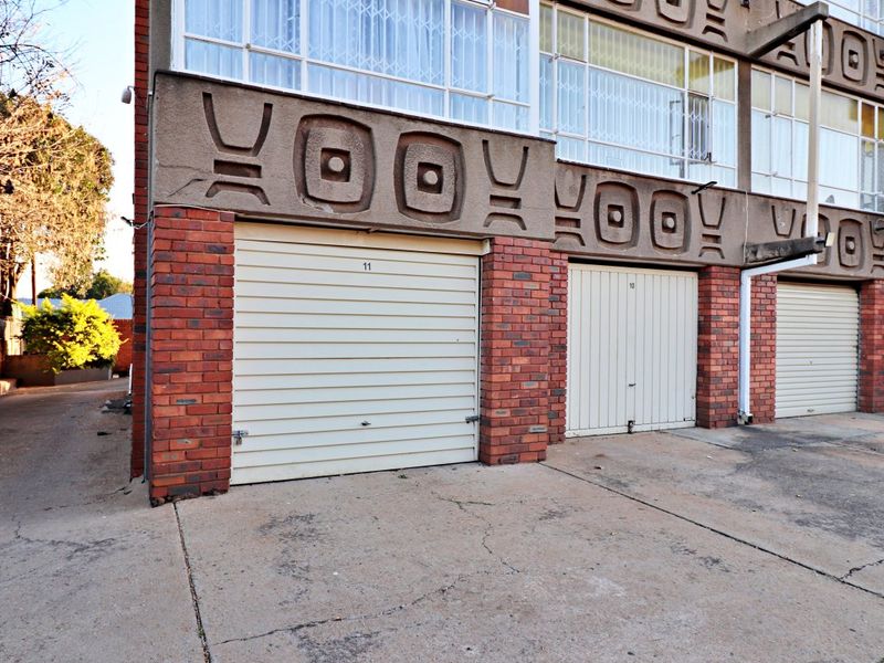Exterior view of apartment complex garage units featuring brick construction, roll-up doors, and decorative concrete architectural detailing.