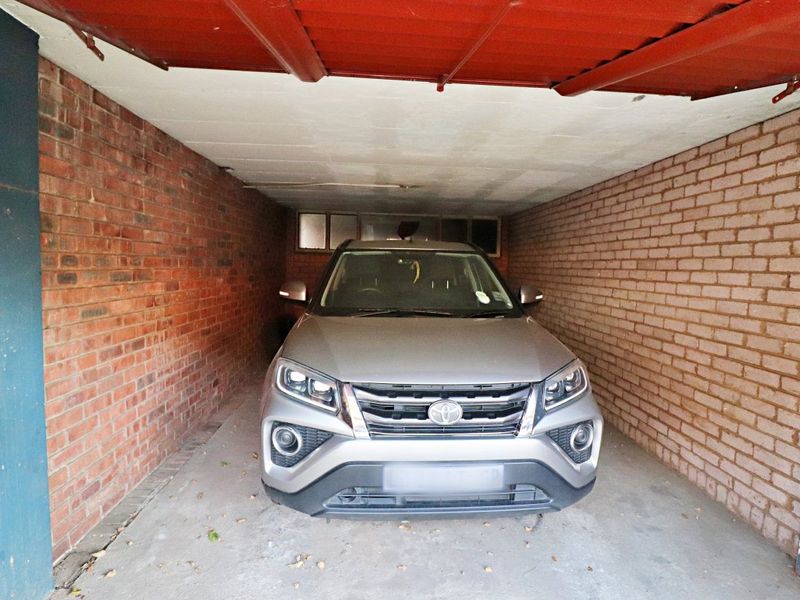 A functional single-car garage featuring exposed brick walls, a concrete floor, and a corrugated metal roof structure.