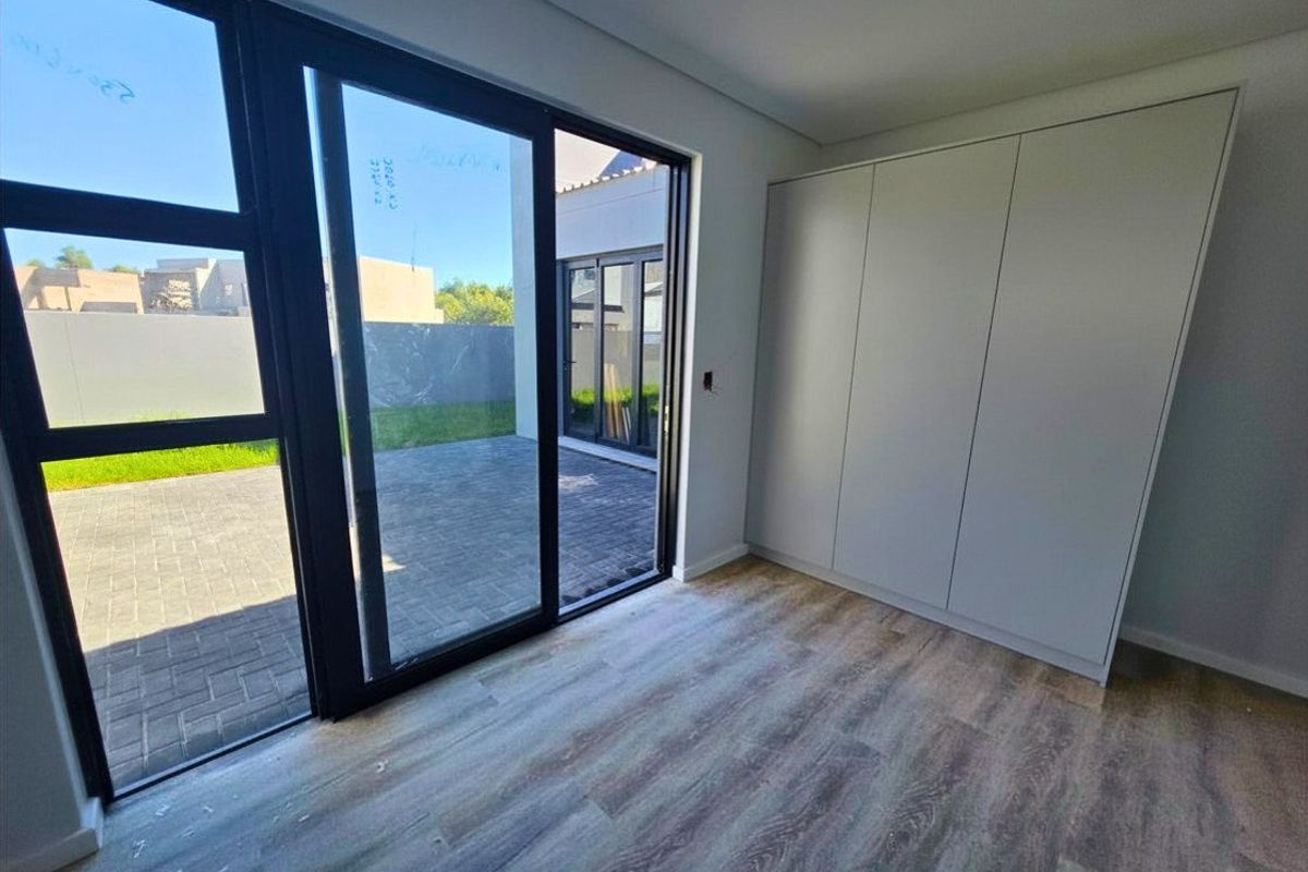 Modern bedroom featuring built-in cupboards, laminate flooring, and large sliding glass doors providing direct access to the paved patio area.