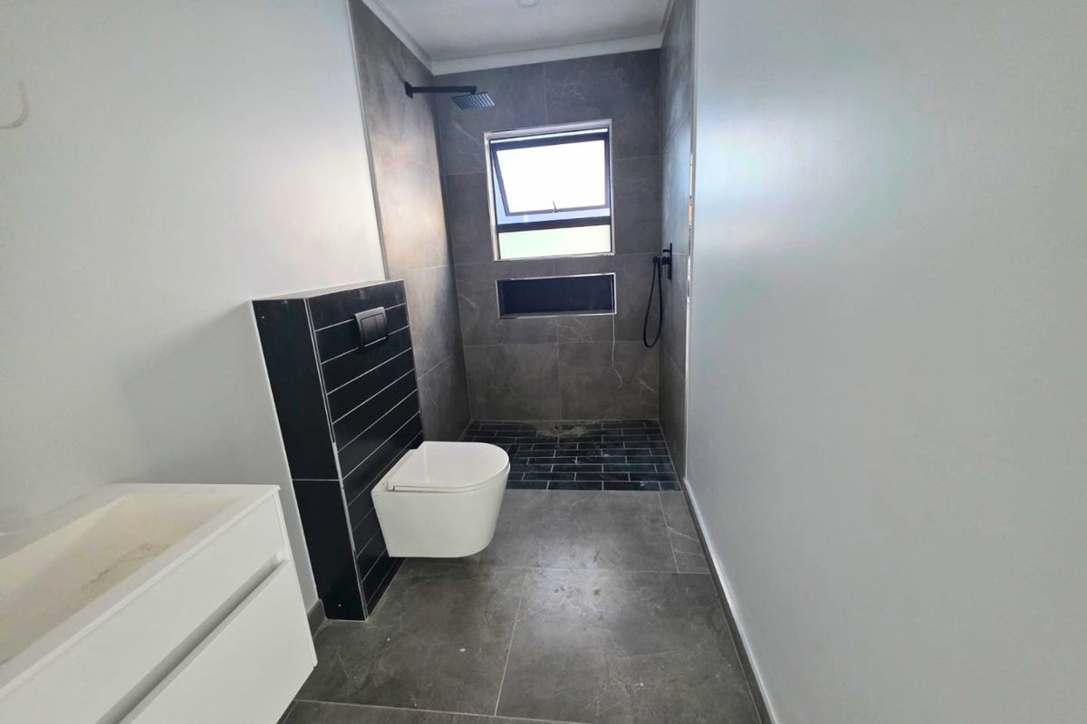 Modern bathroom featuring a wall-mounted toilet, walk-in shower with rain shower head, and contemporary grey tiling throughout.