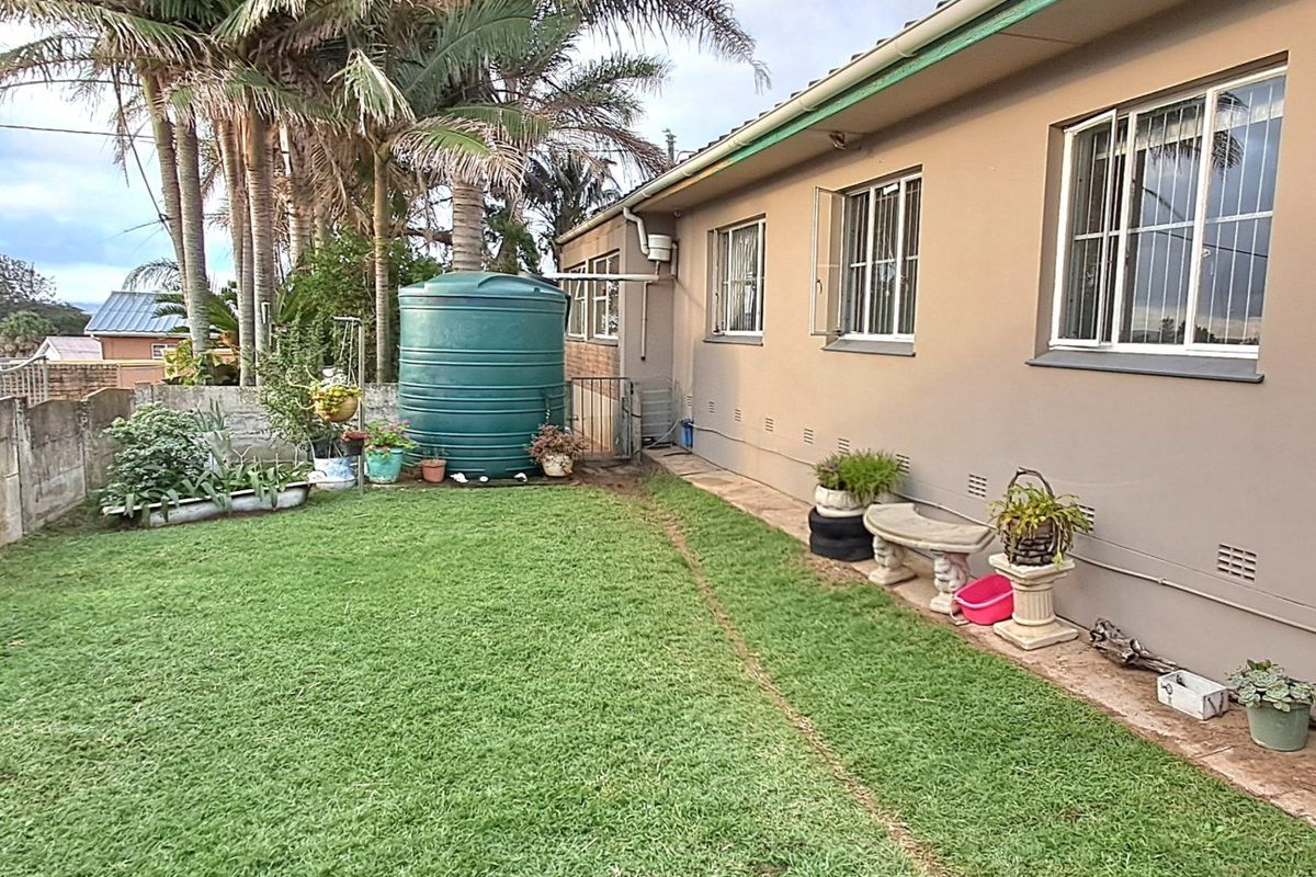 Rear exterior view of the property featuring a lawn, established palm trees, and a large water storage tank.