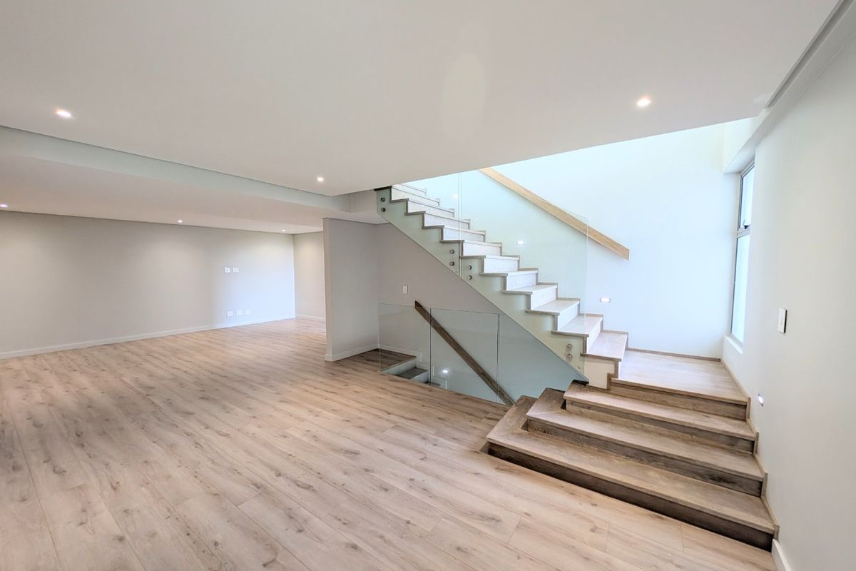 Spacious open-plan living area featuring modern timber laminate flooring, a contemporary staircase with glass balustrades, and recessed lighting.