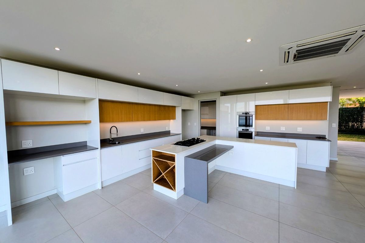 Modern, spacious kitchen featuring high-gloss cabinetry, stone countertops, a central island with gas hob, and integrated appliances in a clean, contemporary open-plan layout.