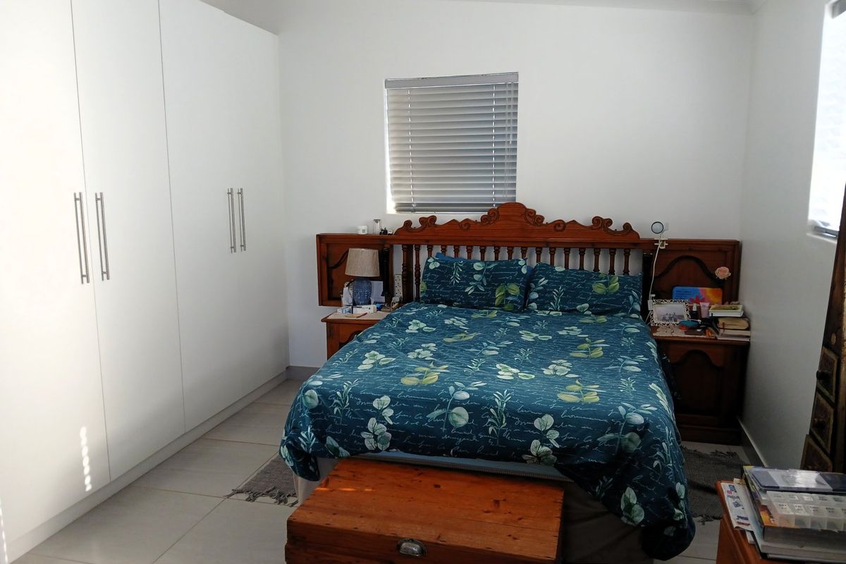 A well-maintained bedroom featuring neutral tiled flooring, ample built-in cupboard storage, and venetian blinds for privacy.