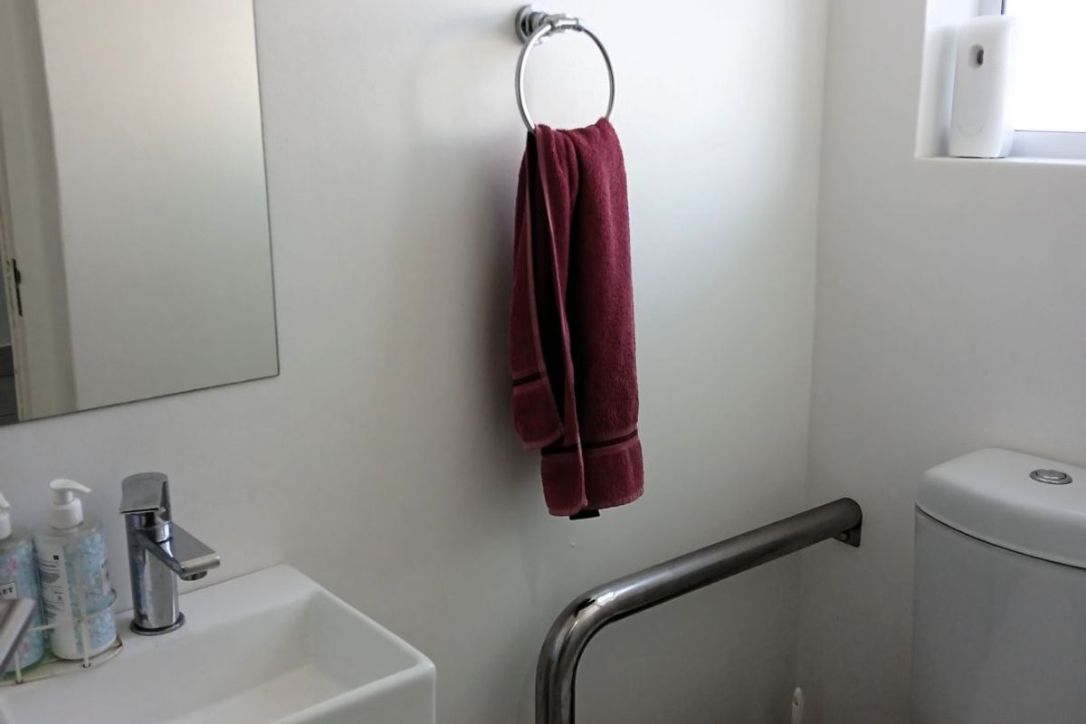 A functional bathroom featuring a wall-mounted basin, chrome mixer tap, toilet, and a safety grab rail.
