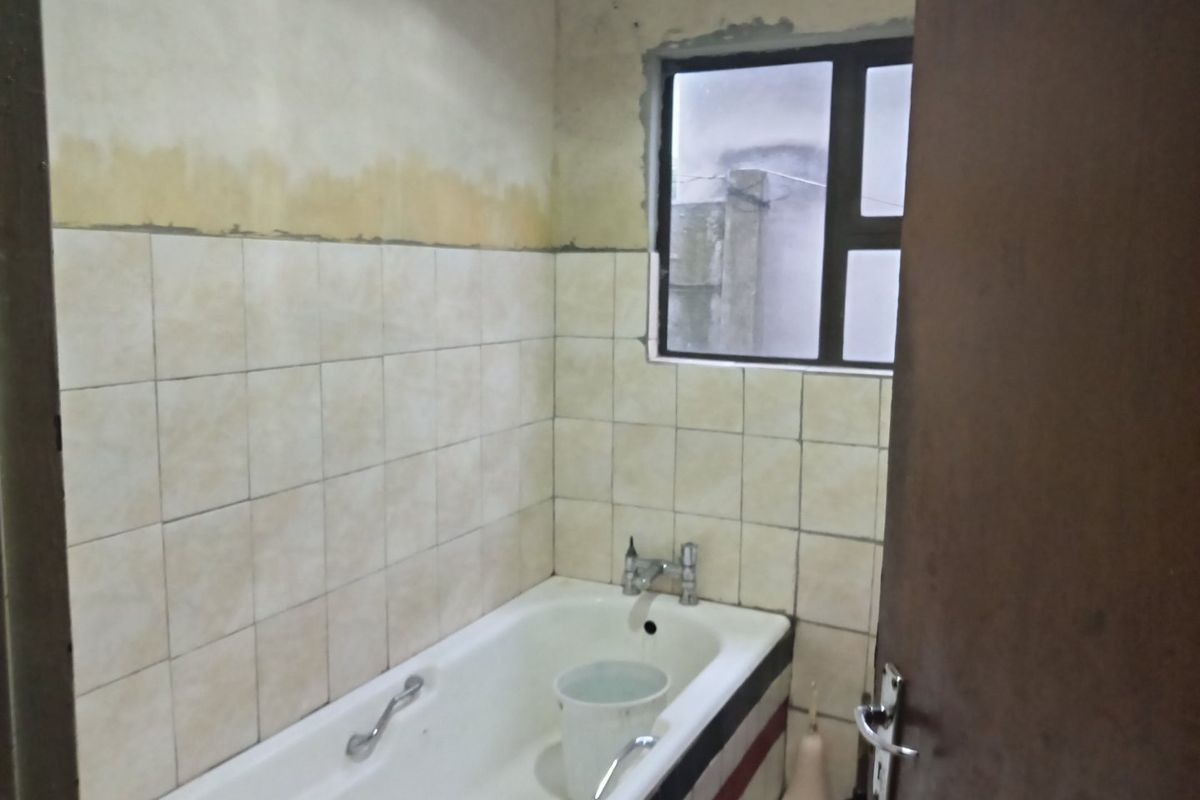A bathroom featuring a bathtub and tiled walls, currently requiring cosmetic updates and finishing work to the wall surfaces.