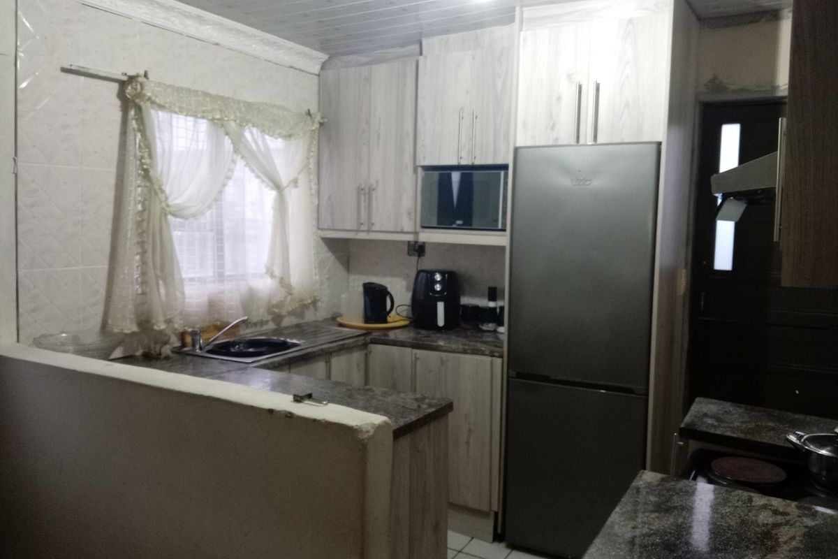 A functional kitchen featuring laminate cabinetry, granite countertops, a built-in microwave, and tiled flooring with a tiled backsplash.
