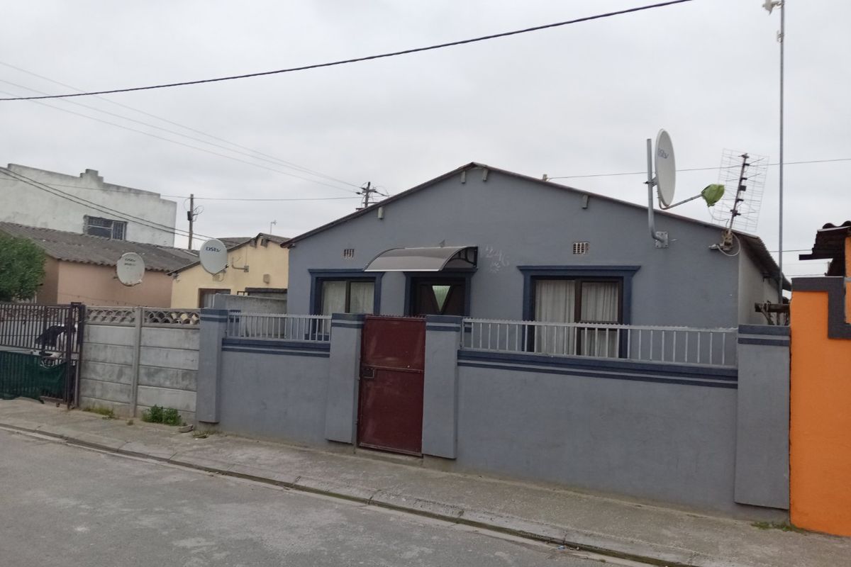 Front exterior view of a single-story house featuring a perimeter wall, metal gate, and satellite dish installation.