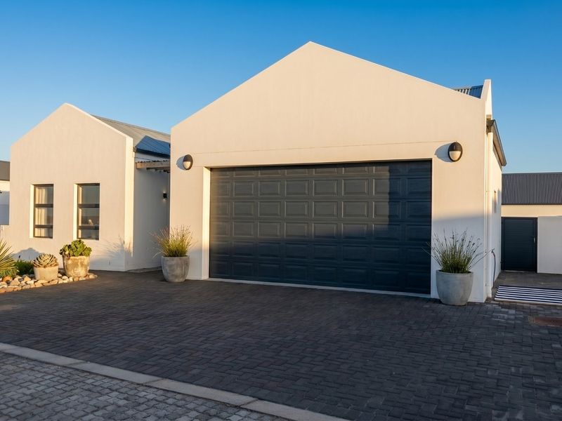 Front elevation of a modern house featuring a paved driveway, a large sectional garage door, and clean white exterior finishes.