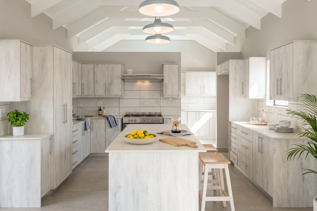 Modern, bright kitchen featuring a central island, light wood-grain cabinetry, vaulted ceilings, and high-quality finishes throughout.