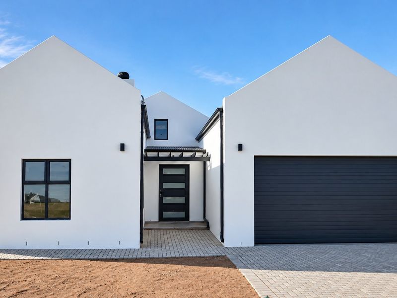 Modern single-story home featuring a clean white facade, gabled rooflines, a double garage, and a paved driveway entrance.