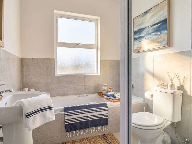 A well-maintained bathroom featuring a pedestal basin, built-in bathtub, and toilet, finished with neutral wall tiling and natural light from a frosted window.