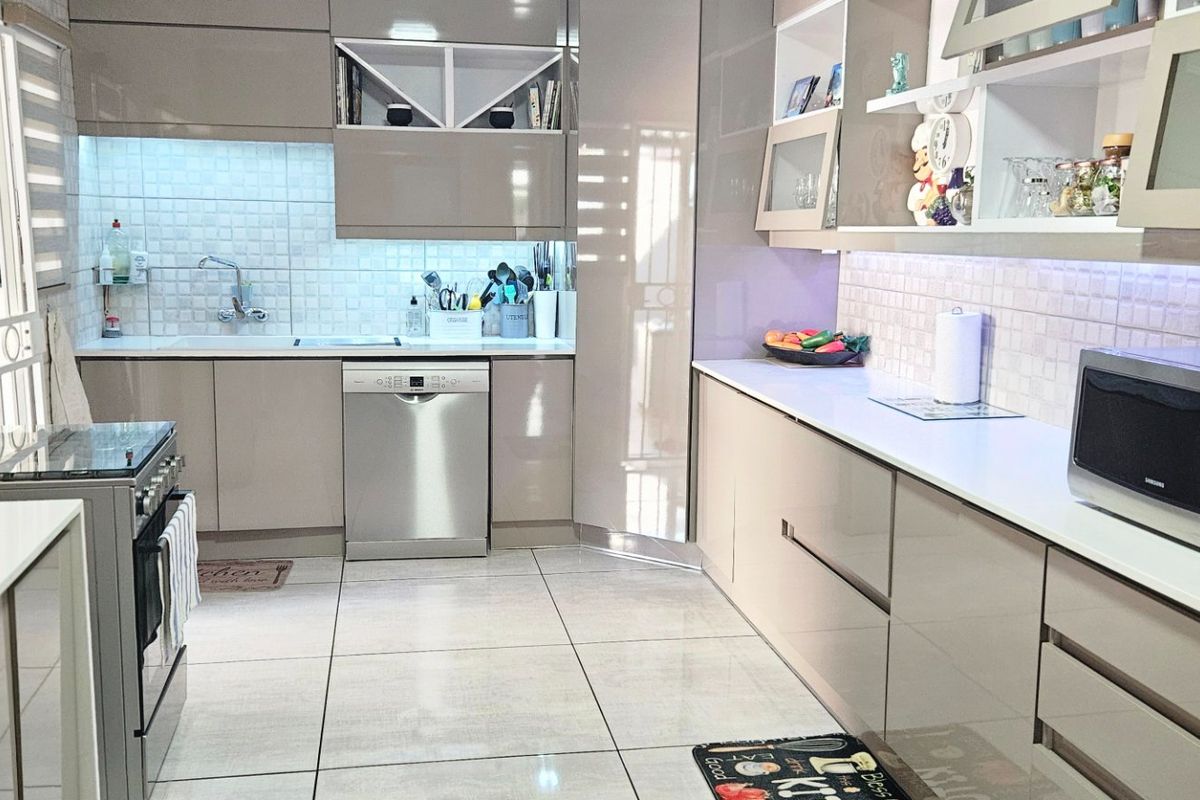 Modern kitchen featuring high-gloss cabinetry, tiled backsplash, integrated dishwasher, built-in microwave, and stainless steel stove with ample counter space.