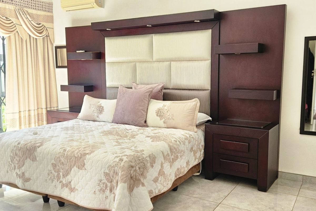 Spacious bedroom featuring tiled flooring, a large built-in headboard with integrated shelving, and direct access to the exterior through a secure sliding door.