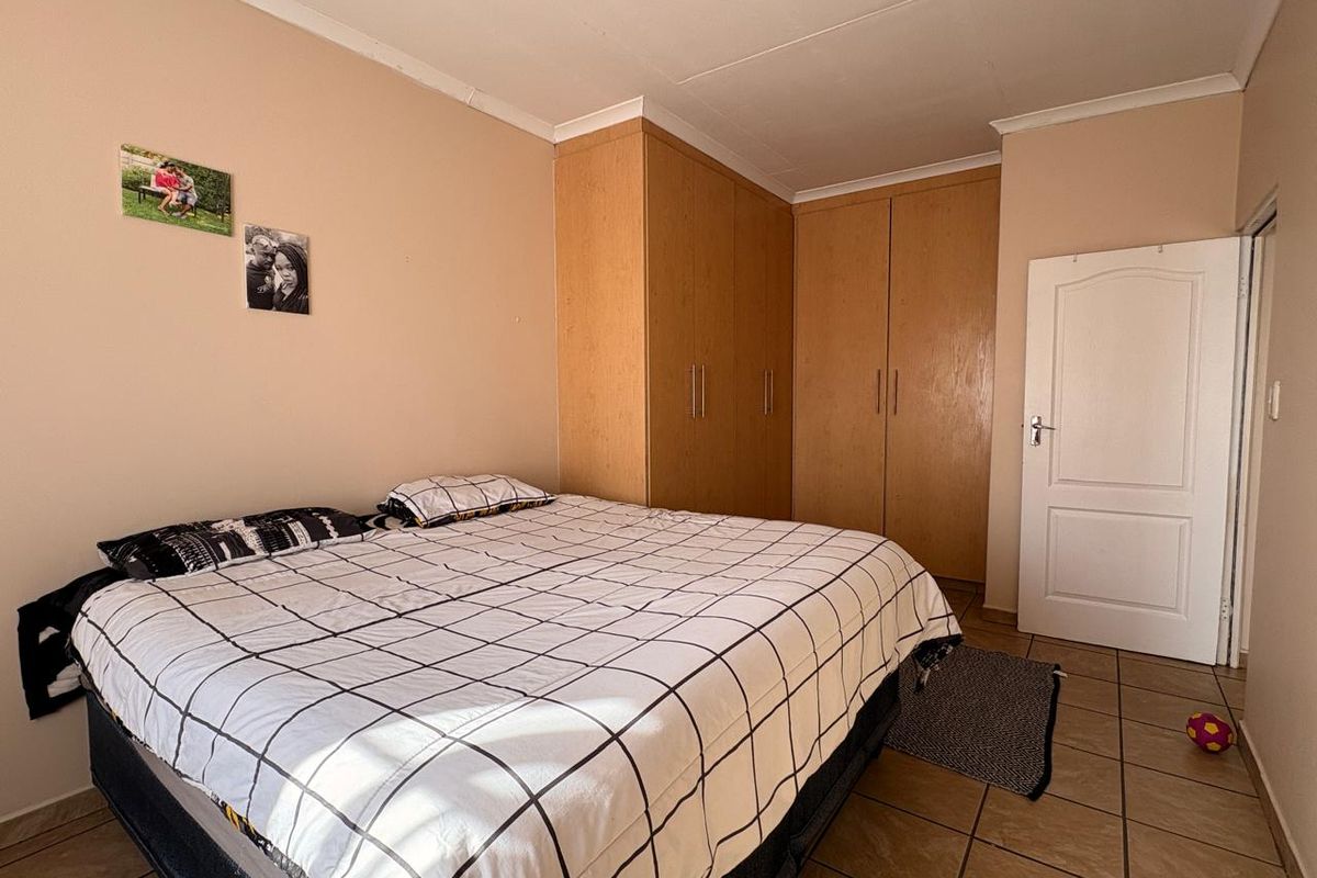 A functional bedroom featuring built-in wooden cupboards, tiled flooring, and coved ceiling details.