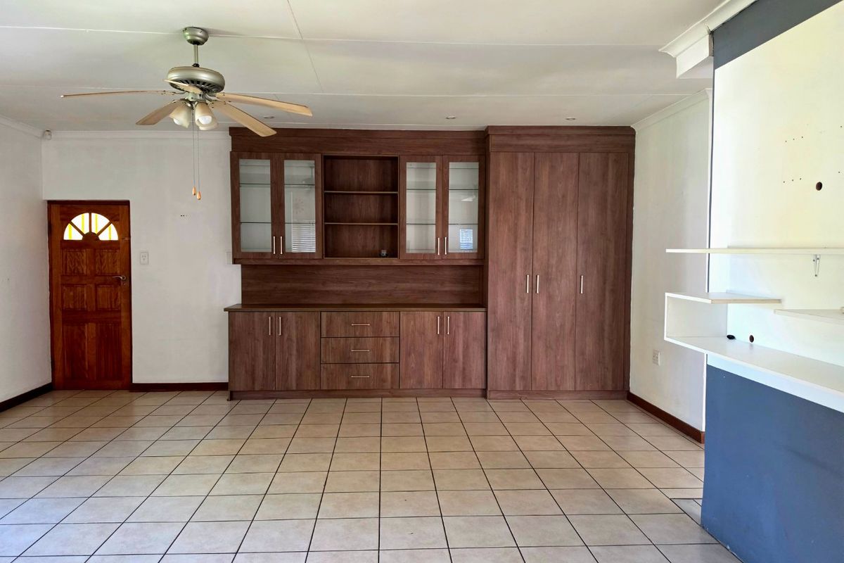 Spacious living area featuring neutral tiled flooring, a ceiling fan, and extensive built-in wooden cabinetry for storage and display.