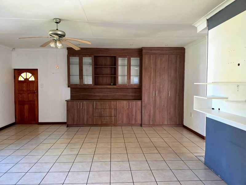 Spacious living area featuring neutral tiled flooring, a ceiling fan, and extensive built-in wooden cabinetry for storage and display.