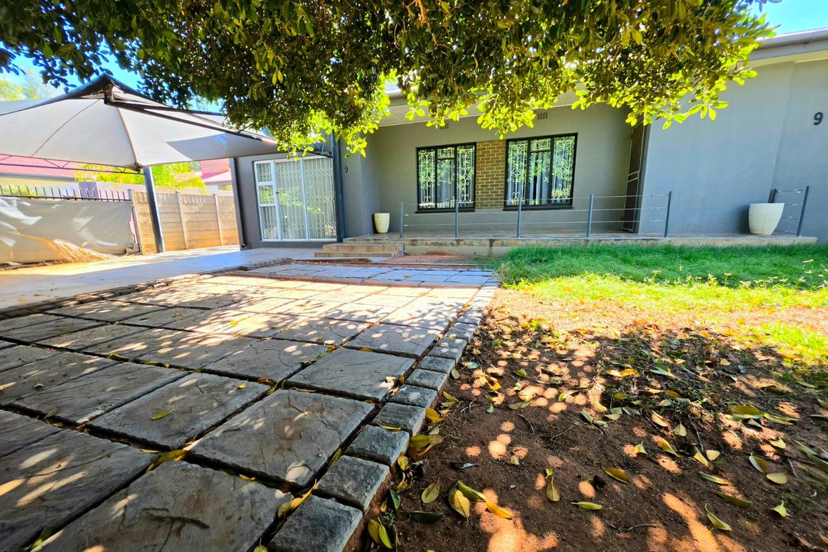 Rear exterior view featuring a paved patio area, security-fitted windows, and a shaded outdoor space with a boundary wall.