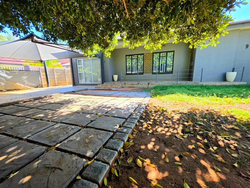 Rear exterior view featuring a paved patio area, security-fitted windows, and a shaded outdoor space with a boundary wall.