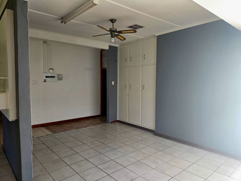 An empty living area featuring tiled flooring, a ceiling fan, and built-in storage cupboards, offering a blank canvas for renovation.