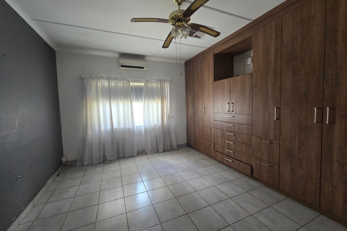 A spacious bedroom featuring extensive built-in wooden cabinetry, tiled flooring, a ceiling fan, and a wall-mounted air conditioning unit.
